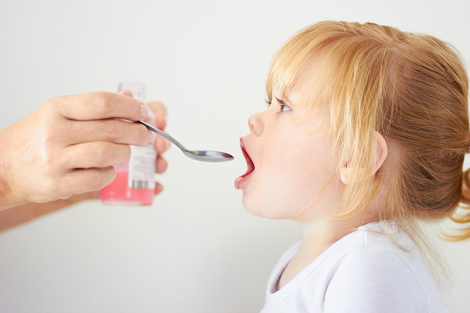 Kleines Mädchen mit offenem Mund erhält einen Löffel mit Arzneimittel